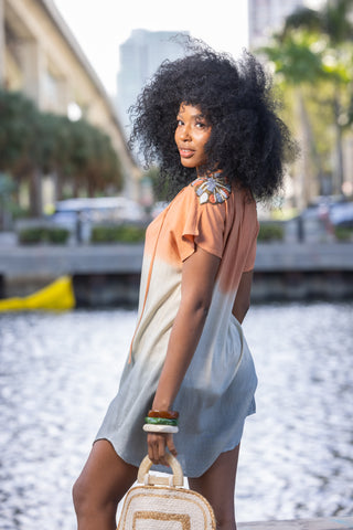 Woman in a light dress holding a handbag by a waterfront with blurred background