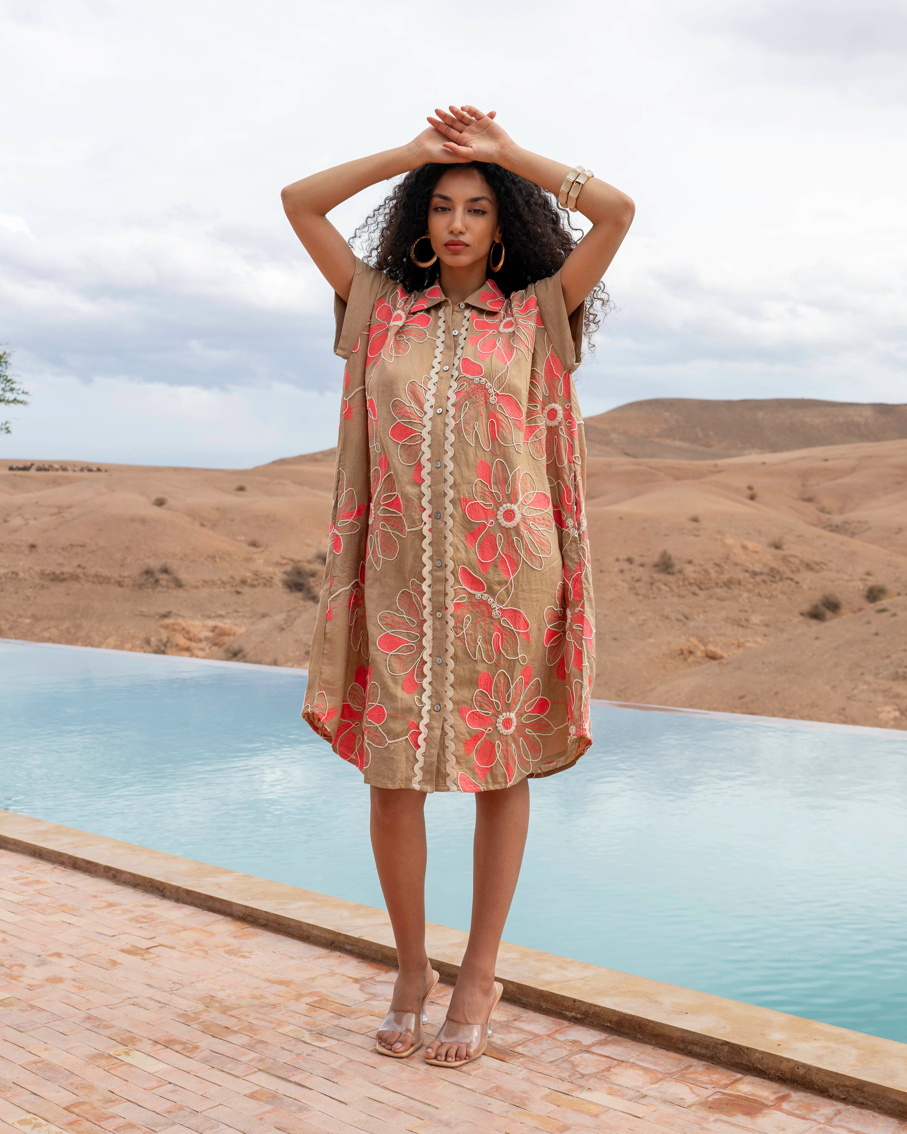 Woman in a floral dress standing by a pool with mountains in the background