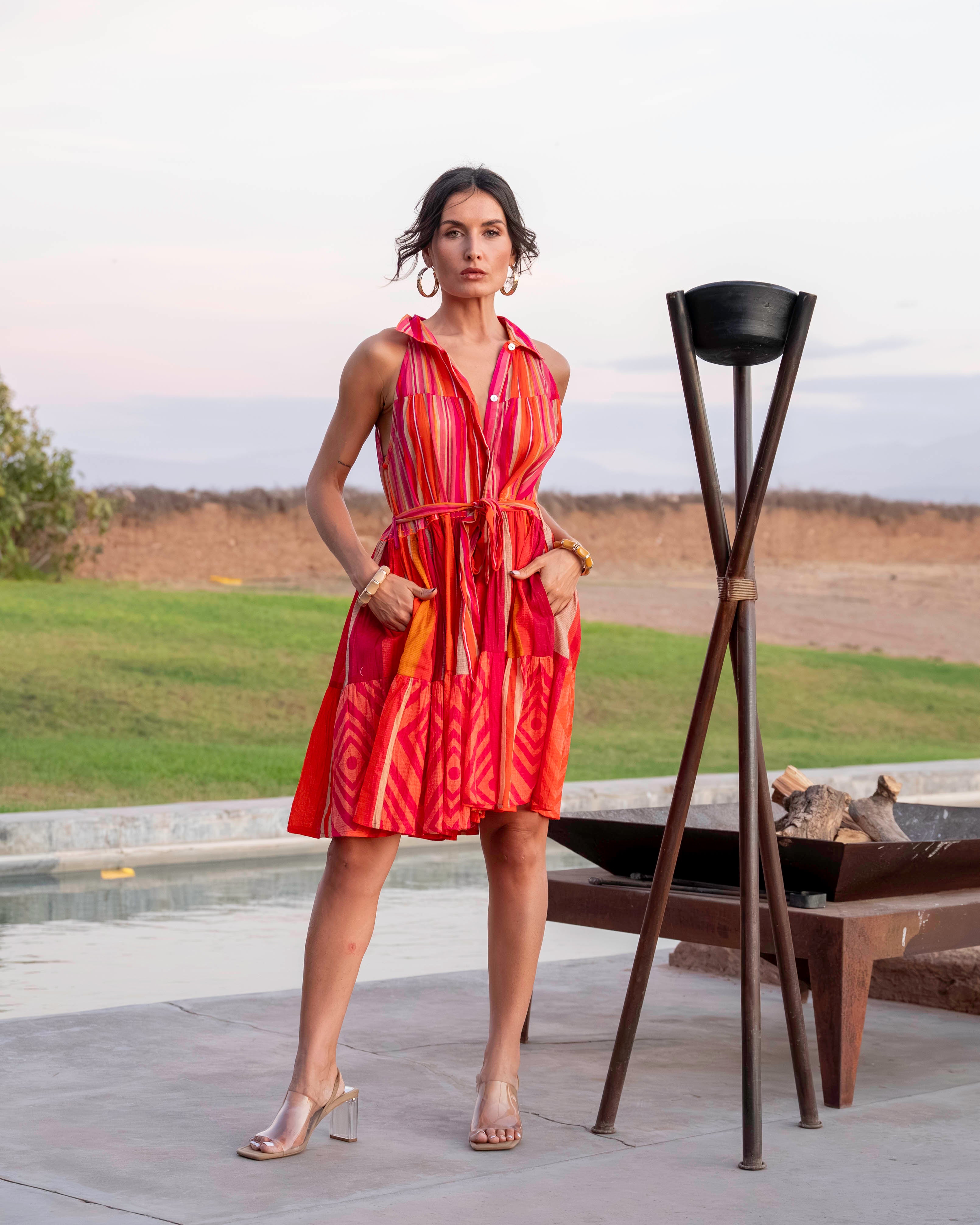 Woman in an orange dress standing outdoors near a pool with a scenic background