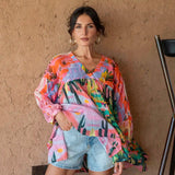 Woman wearing a colorful patterned top and denim shorts against a beige wall.