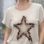 Woman wearing a beige t-shirt with a star design, standing outdoors.
