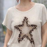Woman wearing a beige t-shirt with a star design, standing outdoors.