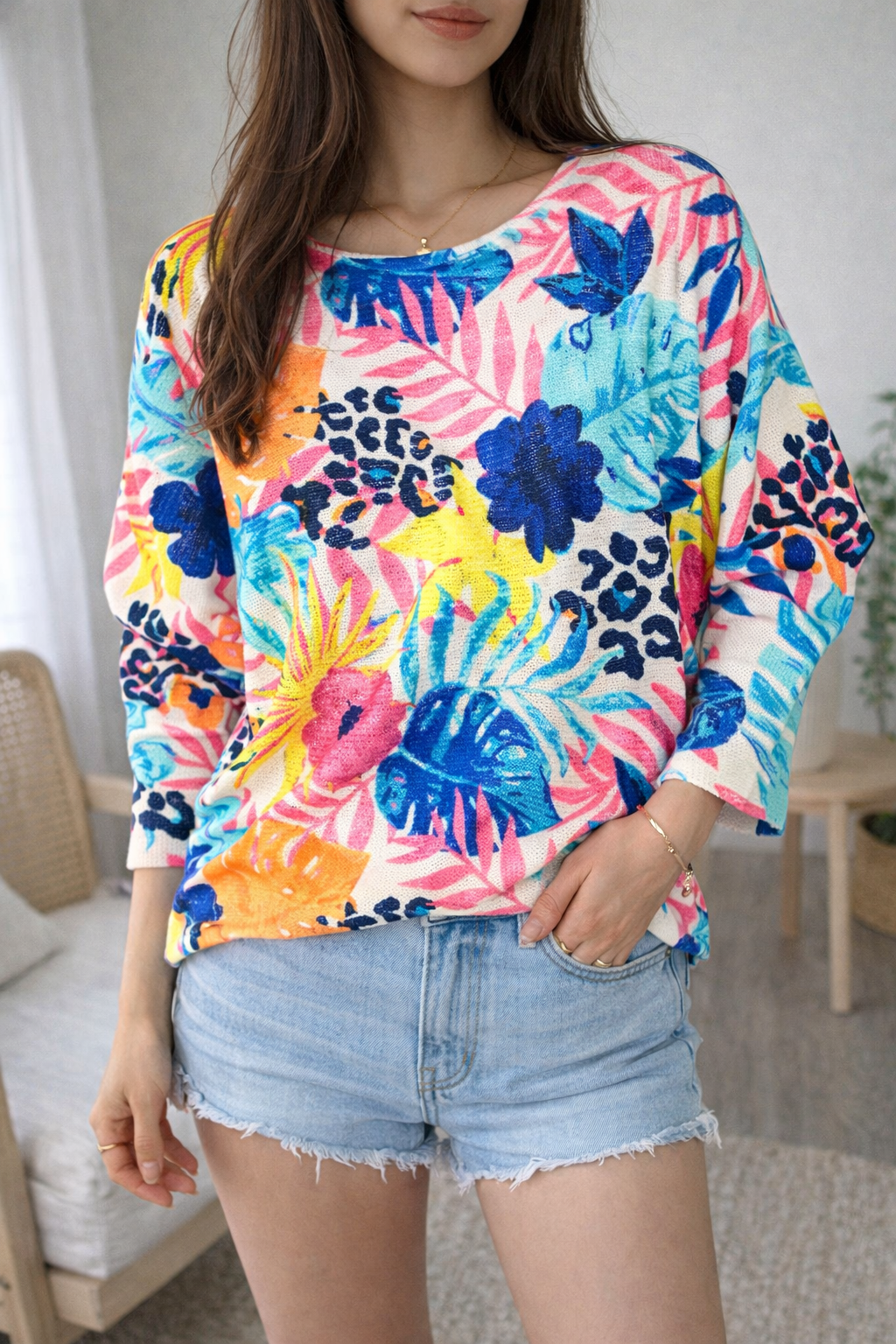 Person wearing a colorful floral and leopard print top with denim shorts indoors.