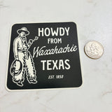Sticker with 'Howdy from Waxahachie Texas' text and a cowboy graphic on a marble surface.