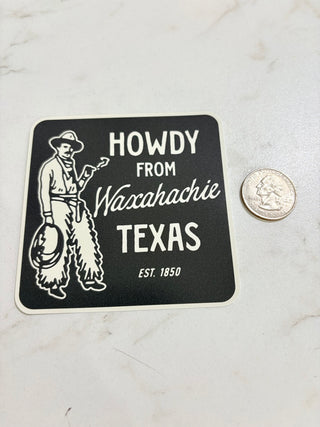 Sticker with 'Howdy from Waxahachie Texas' text and a cowboy graphic on a marble surface.