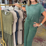 Woman in a green jumpsuit standing in a clothing store with racks of clothes in the background.