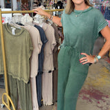 Woman in a green jumpsuit standing in a clothing store with racks of clothes in the background.