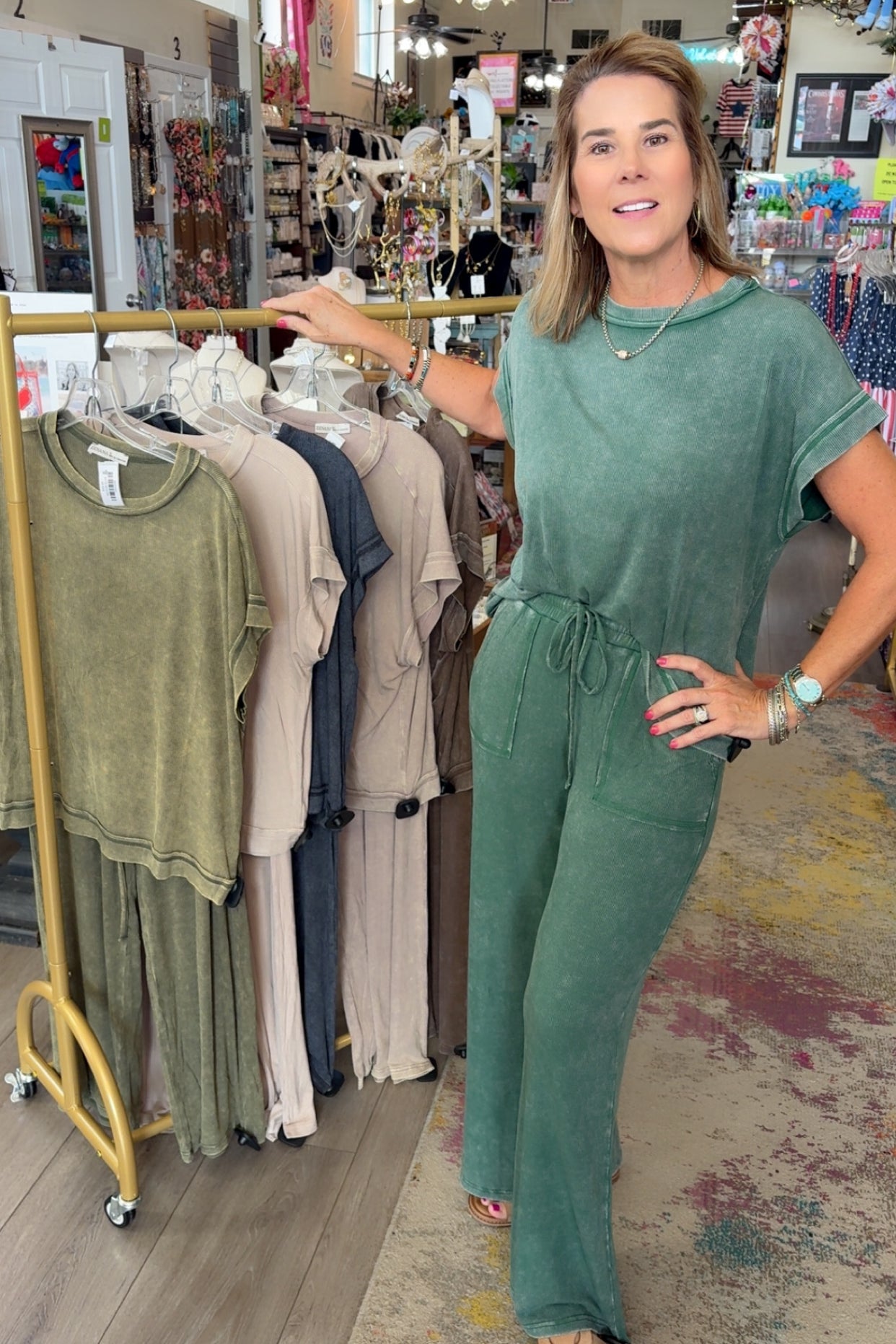 Woman in a green jumpsuit standing in a clothing store with racks of clothes in the background.