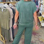 Woman in a green outfit walking through a store with racks of clothes.