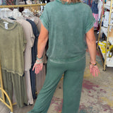 Woman in a green outfit walking through a store with racks of clothes.