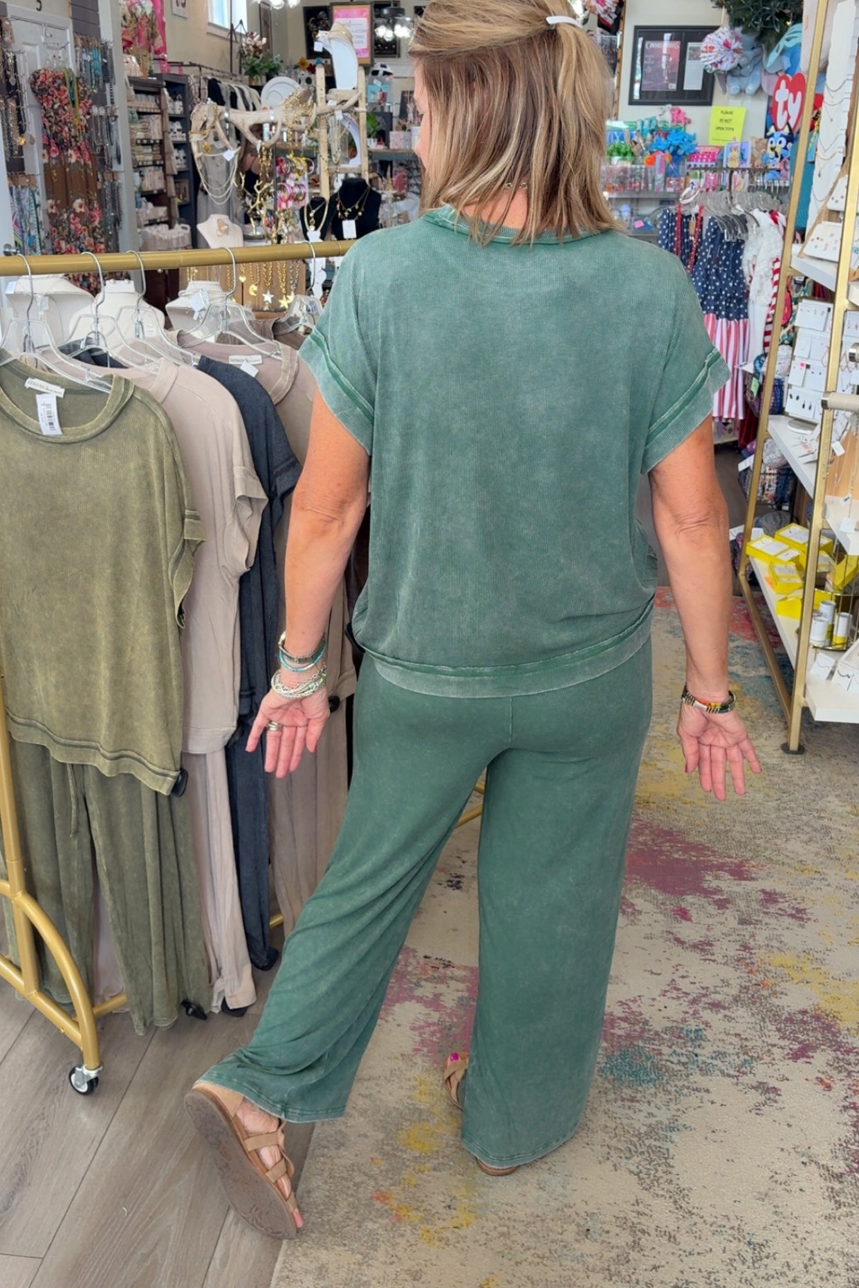 Woman in a green outfit walking through a store with racks of clothes.