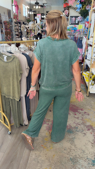 Woman in a green outfit walking through a store with racks of clothes.