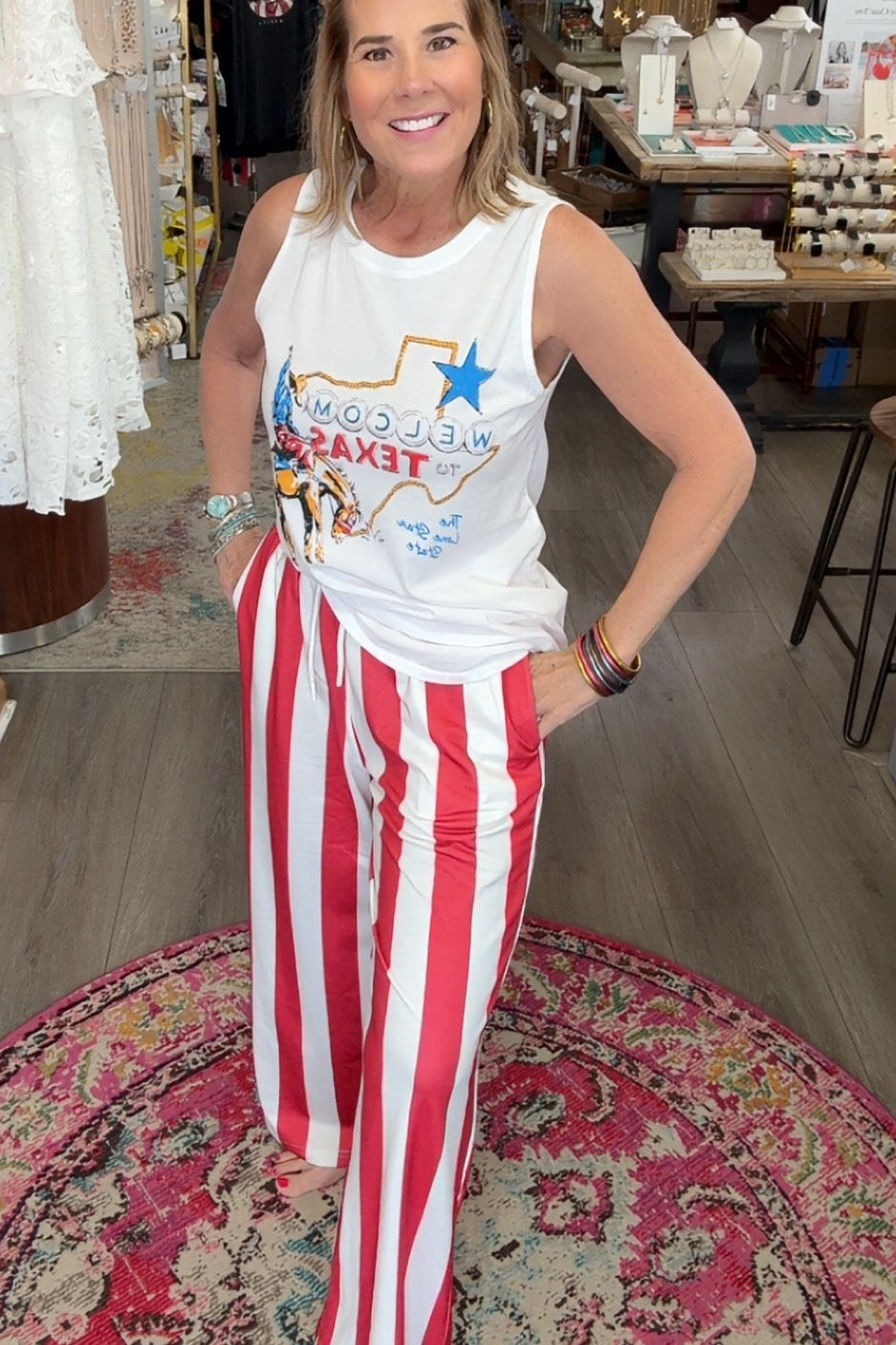 Woman in a store wearing a white tank top with text and red and white striped pants.
