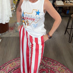 Woman in a store wearing a white tank top with text and red and white striped pants.