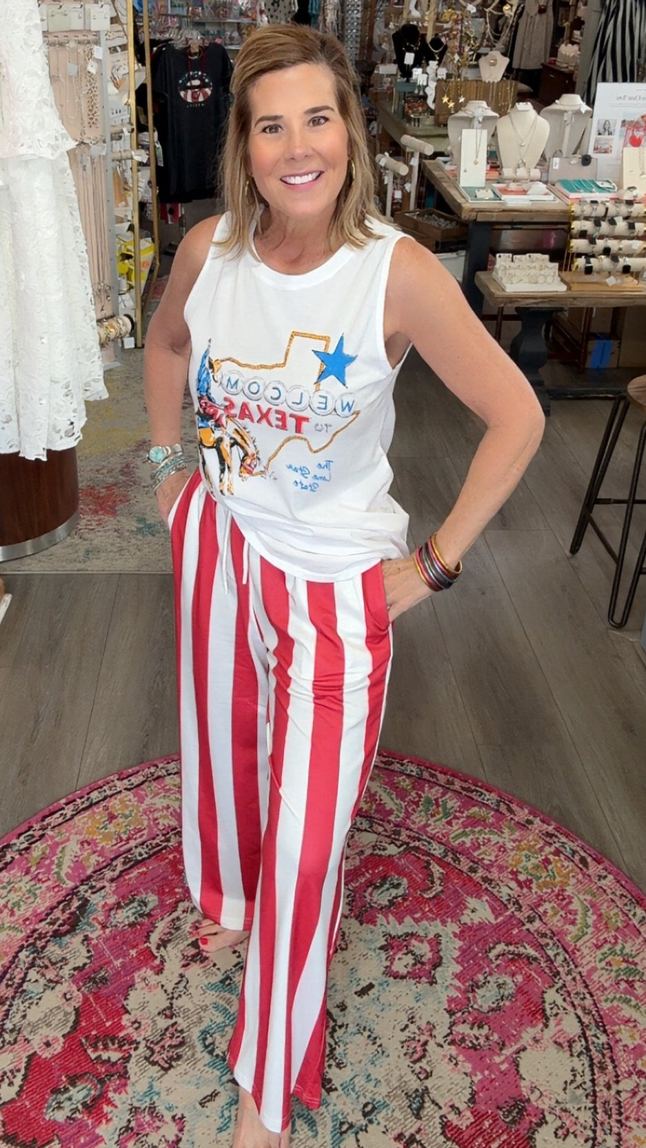Woman in a store wearing a white tank top with text and red and white striped pants.