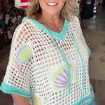 Woman wearing a crochet top with shell patterns in a store setting