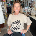 Woman holding a black t-shirt with a white horse design in a store setting