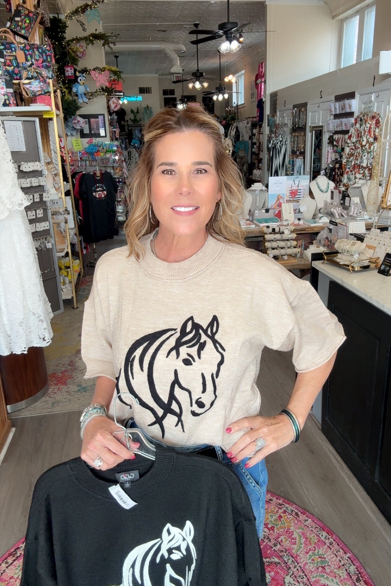 Woman holding a black t-shirt with a white horse design in a store setting