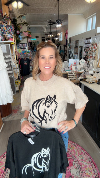 Woman holding a black t-shirt with a white horse design in a store setting