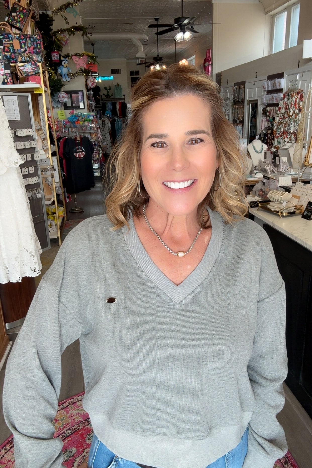 Woman in a gray sweater and blue jeans standing in a store.