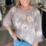 Woman standing in a store with various items on shelves and a colorful rug on the floor.