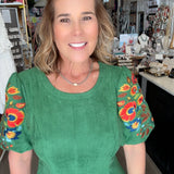 Woman wearing a green top with colorful sleeves in an indoor setting