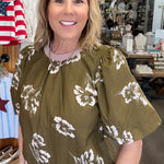 Woman wearing a green blouse with white floral patterns in a store setting.