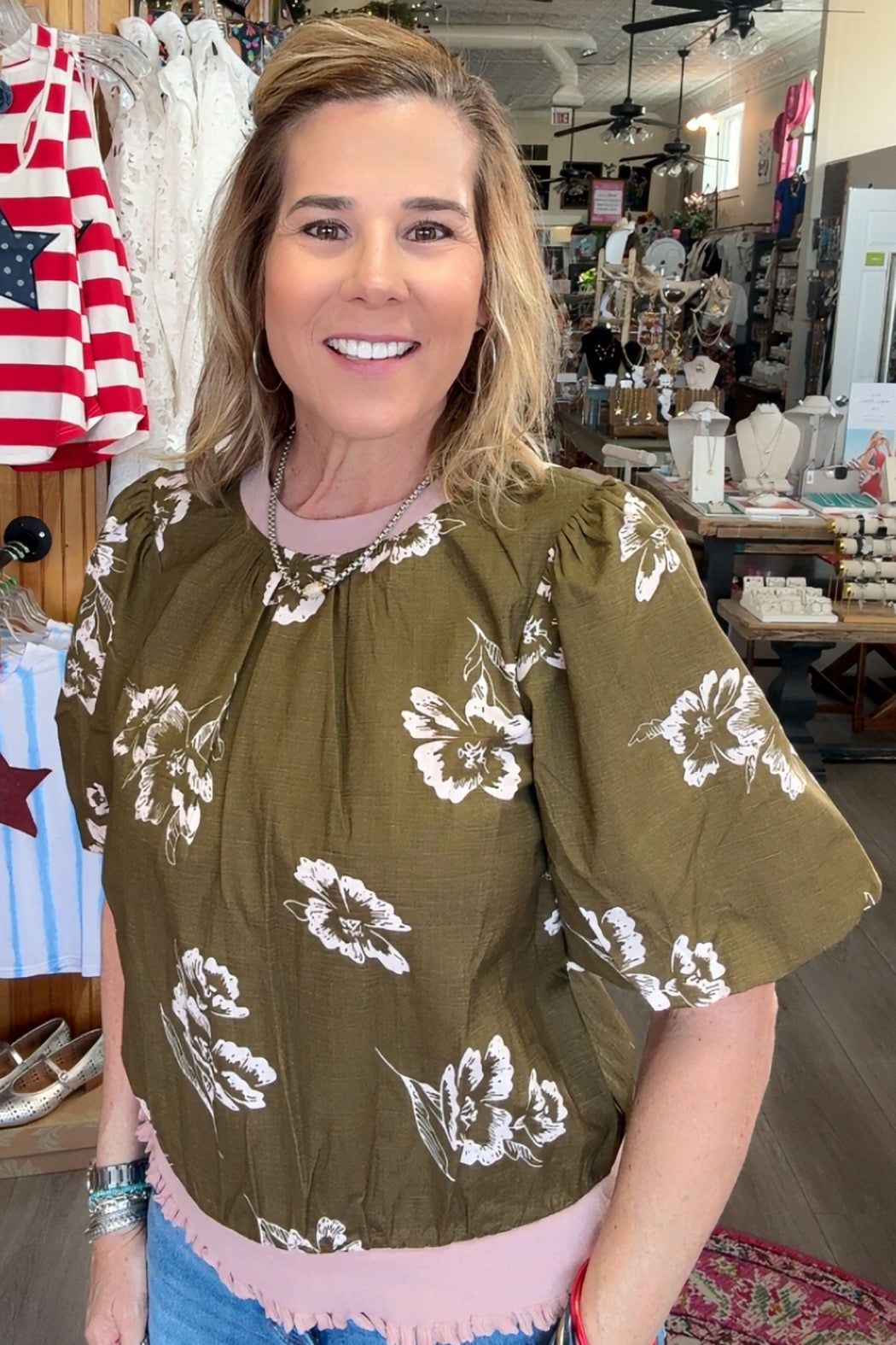 Woman wearing a green blouse with white floral patterns in a store setting.