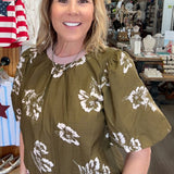 Woman wearing a green blouse with white floral patterns in a store setting.