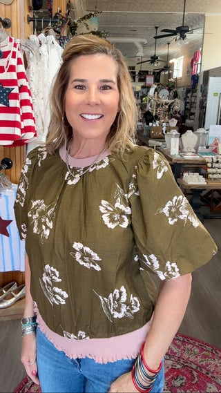 Woman wearing a green blouse with white floral patterns in a store setting.