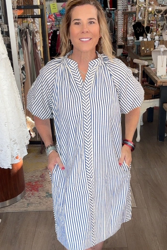 Woman in a striped dress standing in a store with clothing and decor around her.