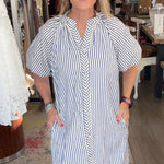 Woman in a striped dress standing in a store with clothing and decor around her.