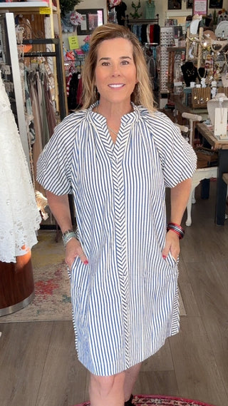 Woman in a striped dress standing in a store with clothing and decor around her.