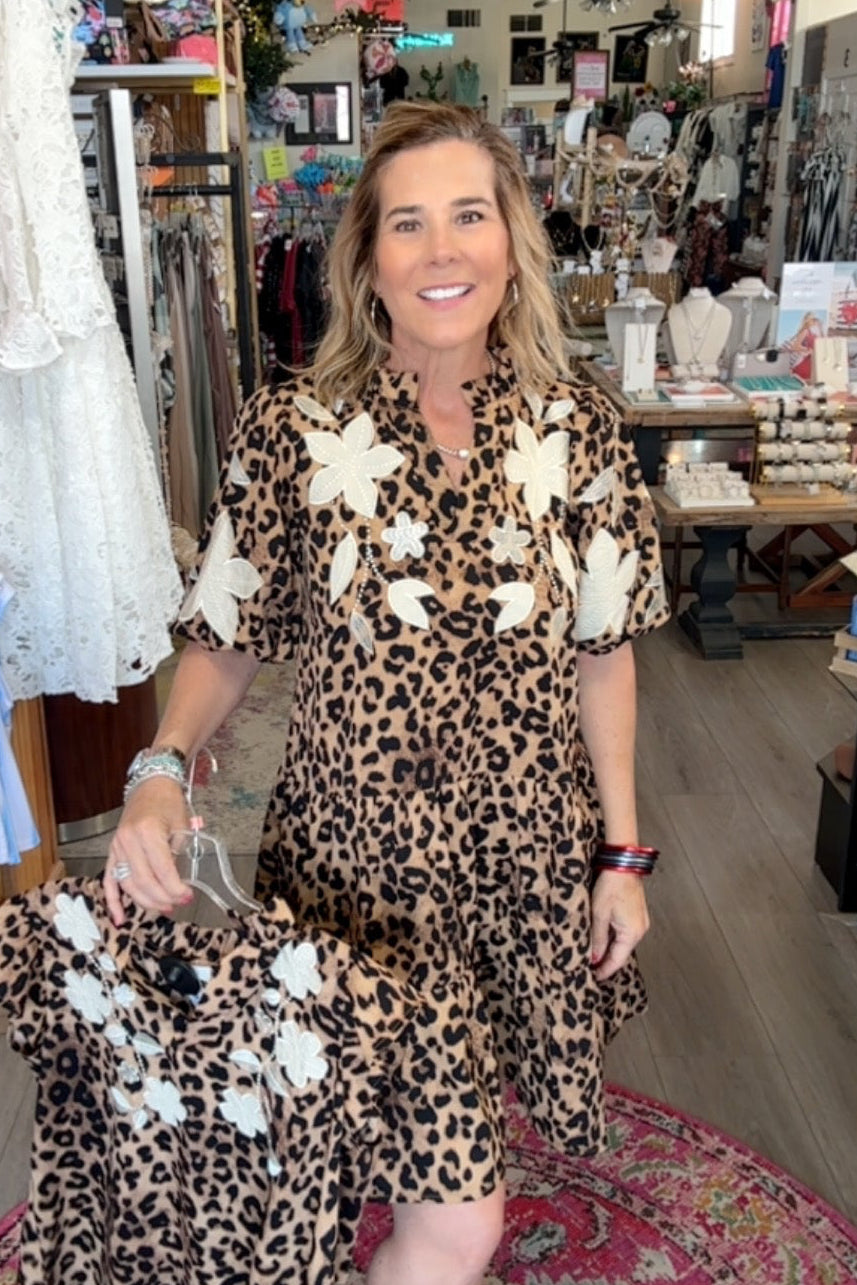 Woman in a leopard print dress with white floral accents standing in a store.