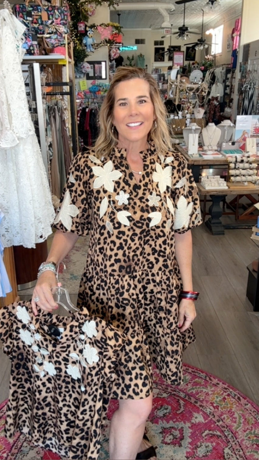 Woman in a leopard print dress with white floral accents standing in a store.