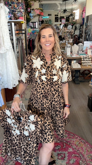 Woman in a leopard print dress with white floral accents standing in a store.