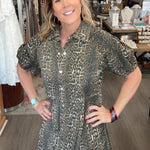 Woman in a patterned dress standing in a store with various items on shelves.