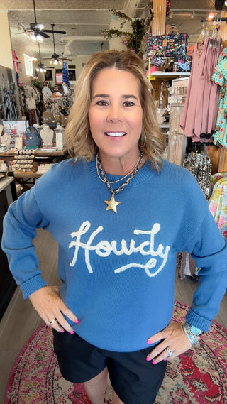 A woman wearing a blue crewneck sweater with 'Floundy' written in white script across the chest, standing in a retail store.