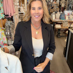 MODEL IN BLACK BLAZER HOLDING A OAT COLORED BLAZER