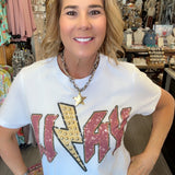 A woman wearing a white graphic t-shirt with a large red and gold 'WAYNE' text design featuring a lightning bolt, standing in a retail store.
