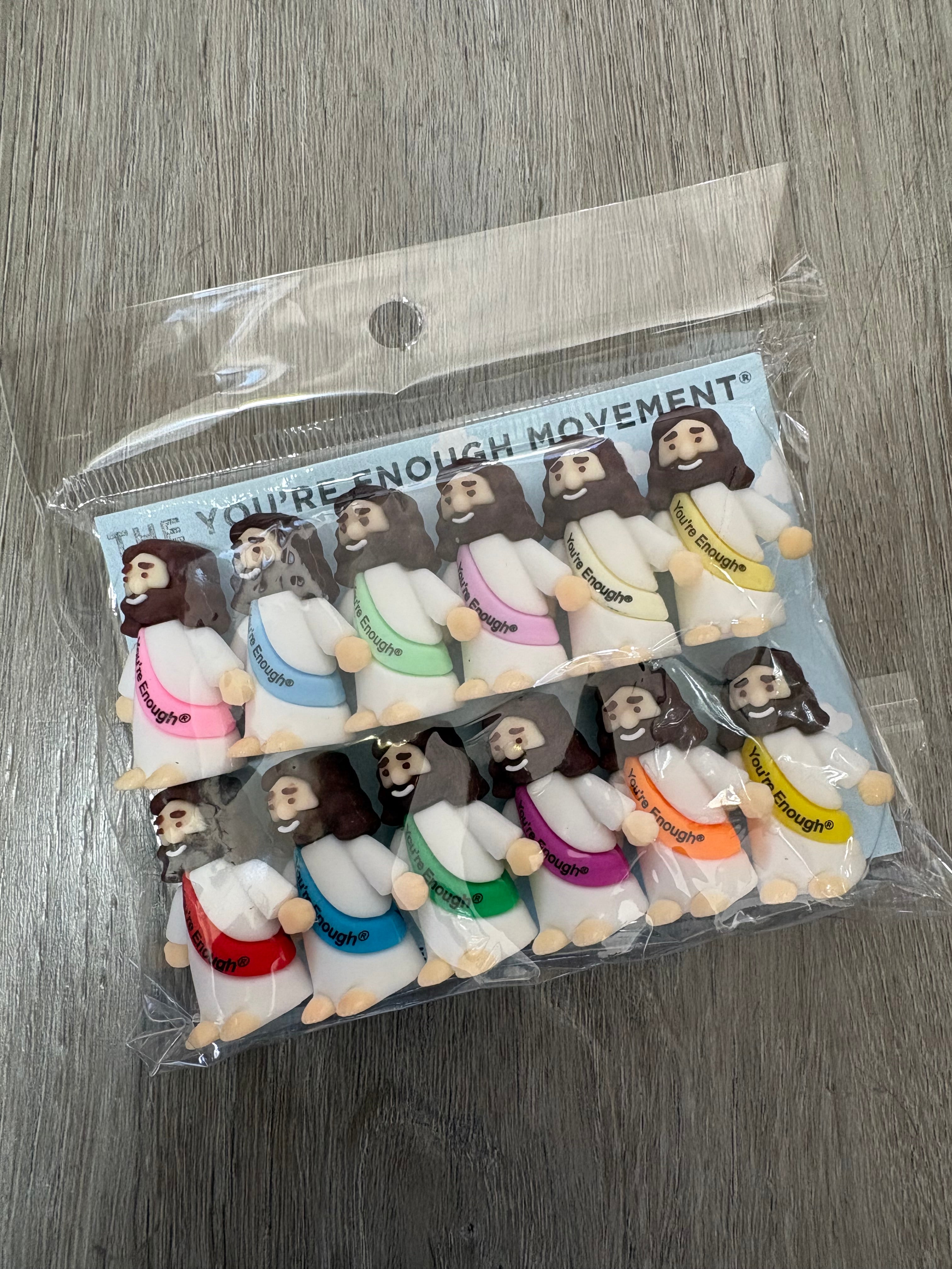 A clear plastic bag containing multiple small plush toy figures arranged in two columns on a gray wood-textured surface. The packaging card reads 'YOU'RE NOT ENOUGH MOVEMENT'.
