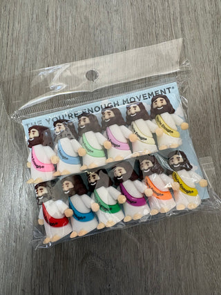 A clear plastic bag containing multiple small plush toy figures arranged in two columns on a gray wood-textured surface. The packaging card reads 'YOU'RE NOT ENOUGH MOVEMENT'.
