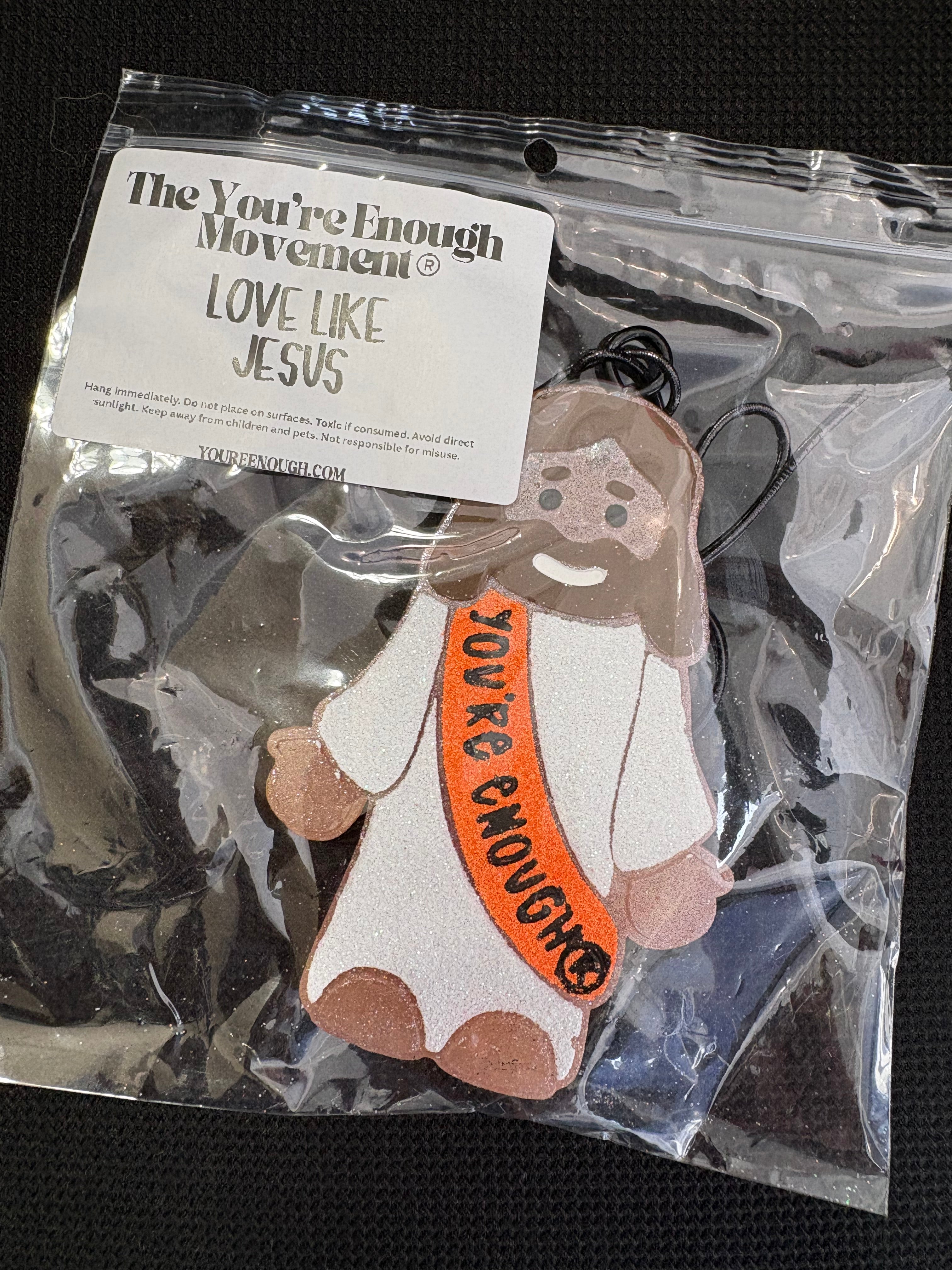 A packaged felt ornament shaped like a cow with the text 'YOU'RE ENOUGH' on its belly, sealed in a clear plastic bag with a printed brand card attached.