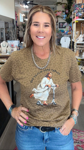 A woman wearing a brown leopard-print graphic t-shirt with a scooter illustration and the text 'EVERY BIRD WORTH A FEELING WRONG' paired with blue jeans, standing inside a retail store.
