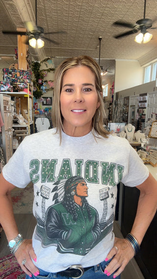 A woman wearing a light gray graphic t-shirt with 'INDIANYS' and a varsity jacket design in green and black, standing in a retail store.