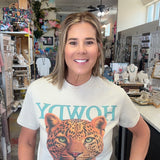 A woman wearing a white graphic t-shirt with a leopard print and turquoise lettering, standing inside a retail store.