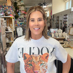 A woman standing inside a boutique shop wearing a white graphic t-shirt with a large leopard print and the word 'VOGUE' printed across the chest.