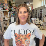 A woman standing inside a boutique shop wearing a white graphic t-shirt with a large leopard print and the word 'VOGUE' printed across the chest.
