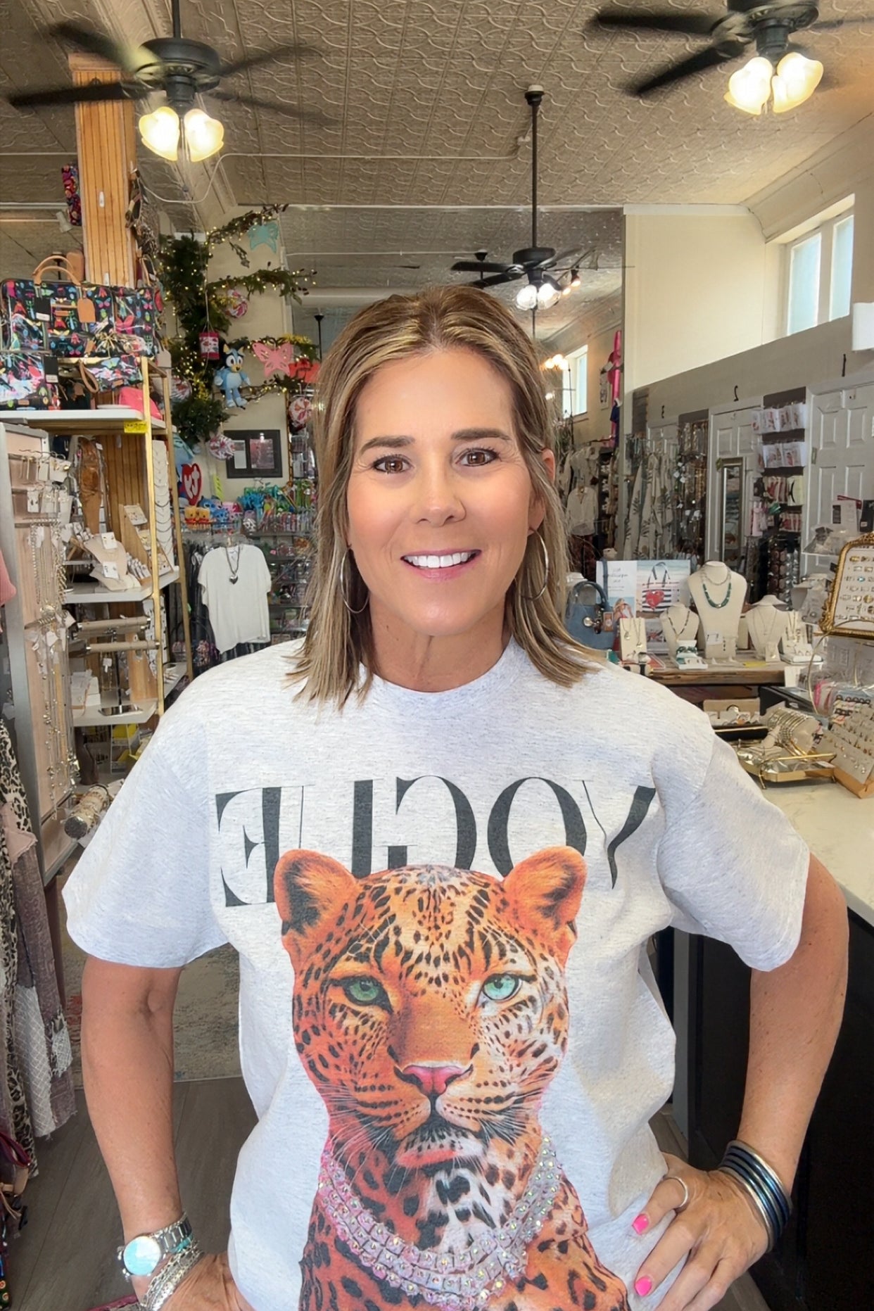 A woman standing inside a boutique shop wearing a white graphic t-shirt with a large leopard print and the word 'VOGUE' printed across the chest.