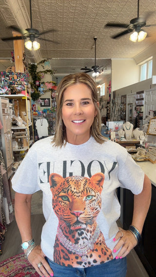 A woman standing inside a boutique shop wearing a white graphic t-shirt with a large leopard print and the word 'VOGUE' printed across the chest.